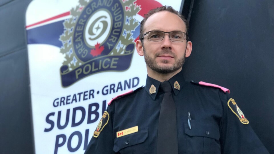 Photo d'un homme portant un uniforme de police noir, le logo de la police de Sudbury en arrière-plan