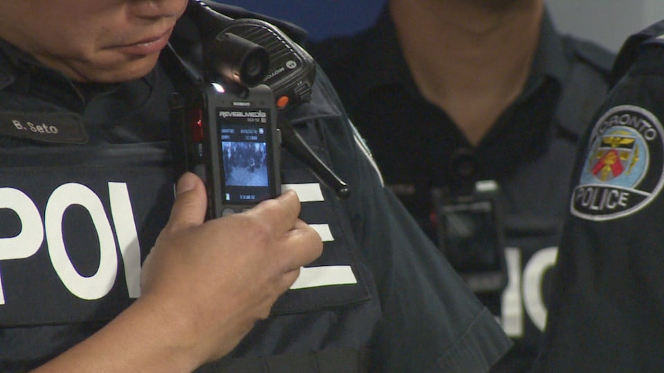 Zoom sur la caméra, plus petite qu'un téléphone cellulaire, sur le gilet d'un policier.