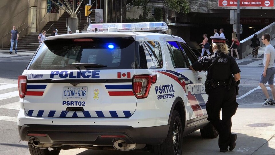 Une policière à côté d'un véhicule de police à une intersection du centre-ville.