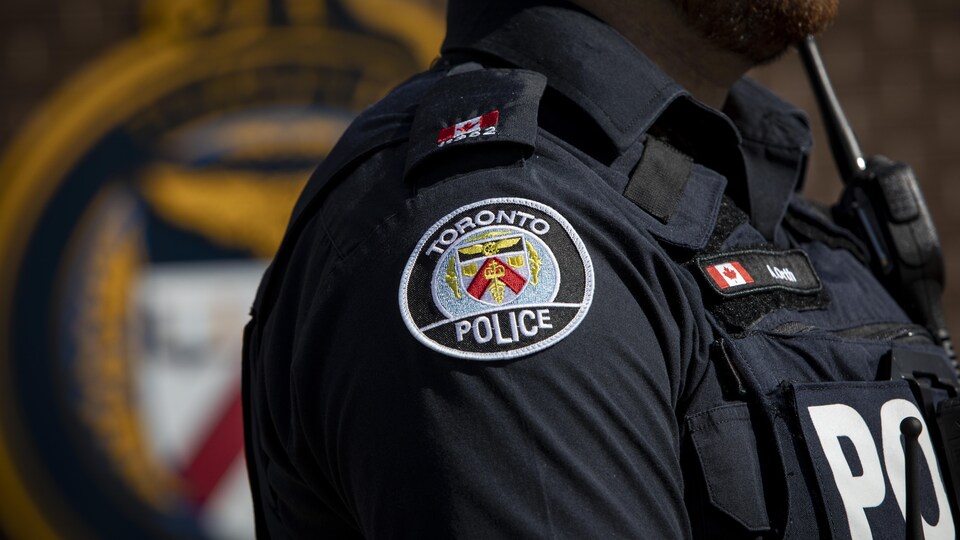 Un policier se tient debout devant le logo du Service de police de Toronto.