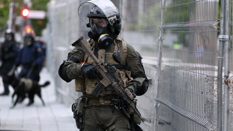Un policier transportant une arme d’assaut dans ses mains monte la garde devant une clôture grillagée.