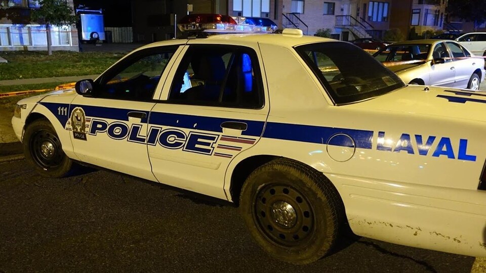 Un policier dans son autopatrouille du Service de police de la ville de Laval, dans un quartier résidentiel, alors que la nuit est tombée.