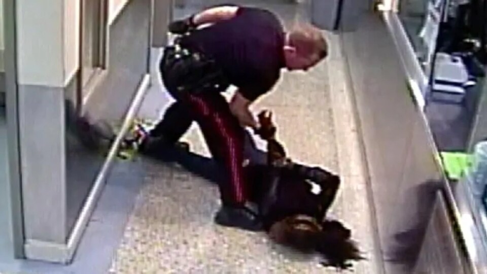 Un policier plaque au sol une femme menottée. 