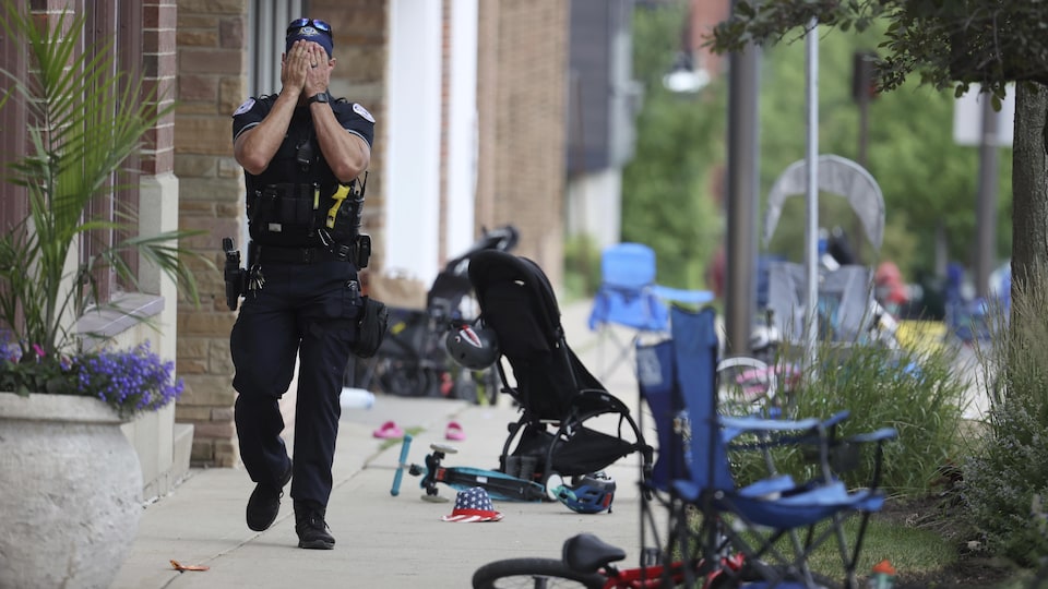 Un policier marche sur un trottoir. Des bicyclettes, des poussettes et des chaises ont été abandonnées près de lui.