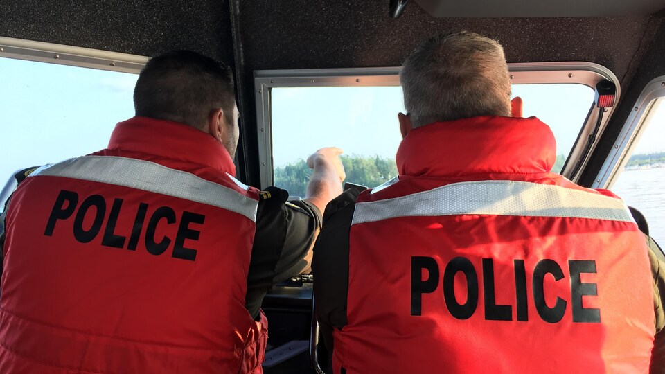 Deux patrouilleurs conduisent un bateau de la Sûreté du Québec à l'occasion d'une opération.