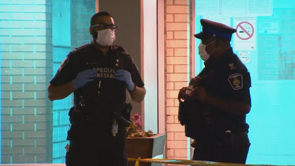 Deux policiers qui portent un masque devant l'entrée d'un édifice, la nuit.