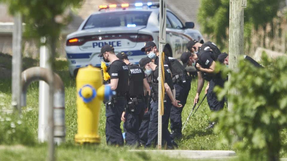Une rangée de policiers travaillent en bordure de route, tandis qu'on voit une voiture de la police de London à l'arrière.