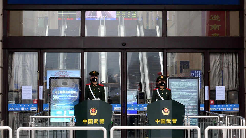 Deux officiers masqués montent la garde devant une gare de train.