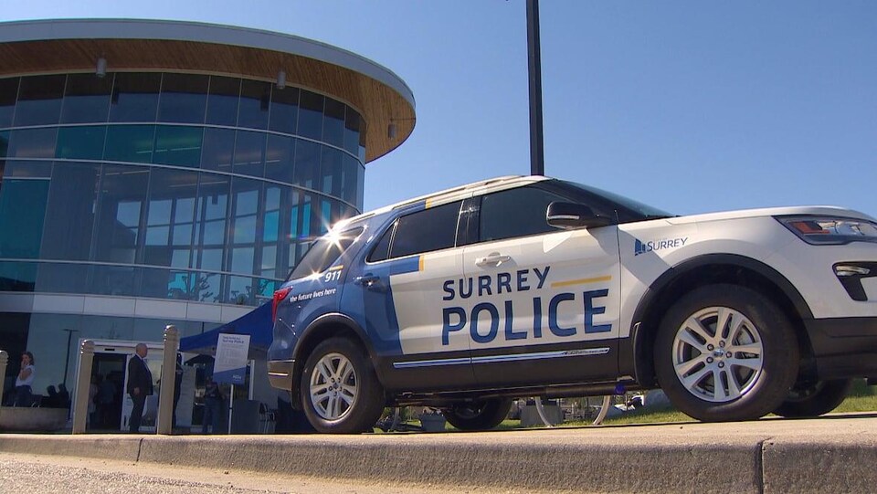 Une voiture de police de Surrey devant un édifice en verre. 
