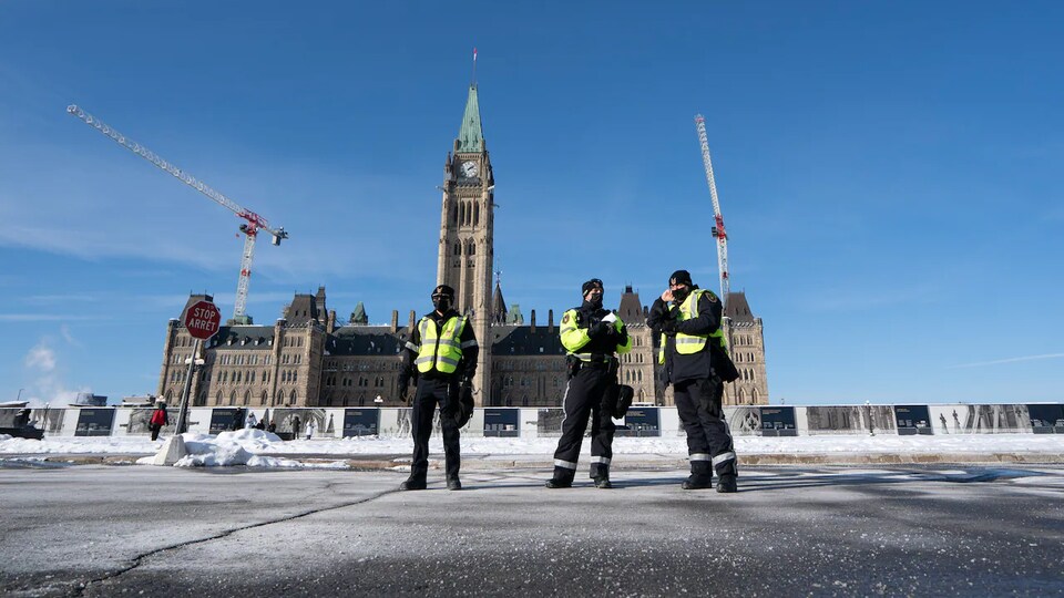 Des agents de protection du Service de protection parlementaire devant le parlement du Canada, en hiver.