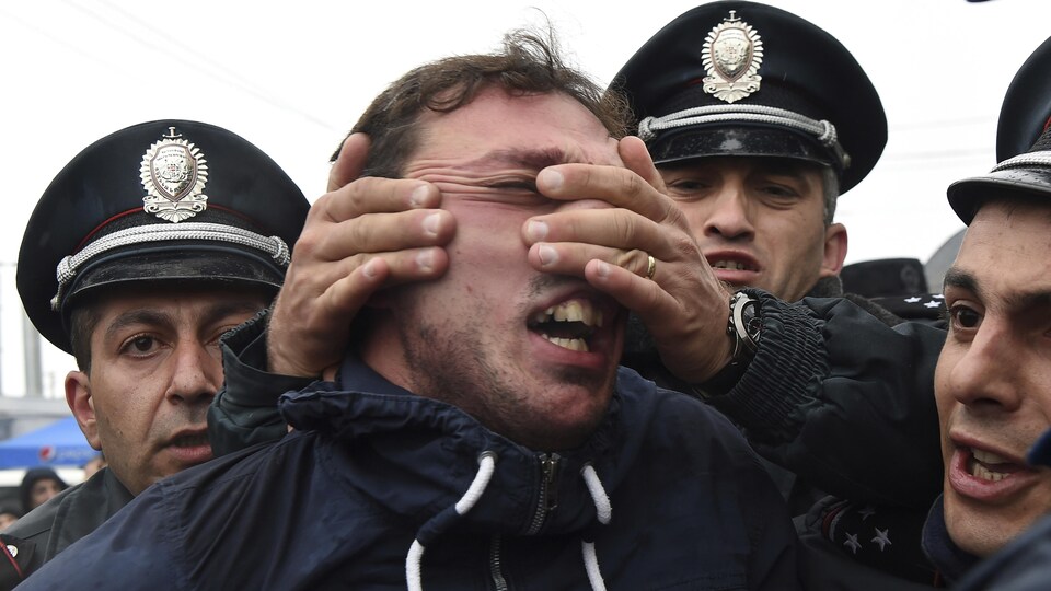 Un policier tente de retenir un manifestant en lui agrippant le visage.