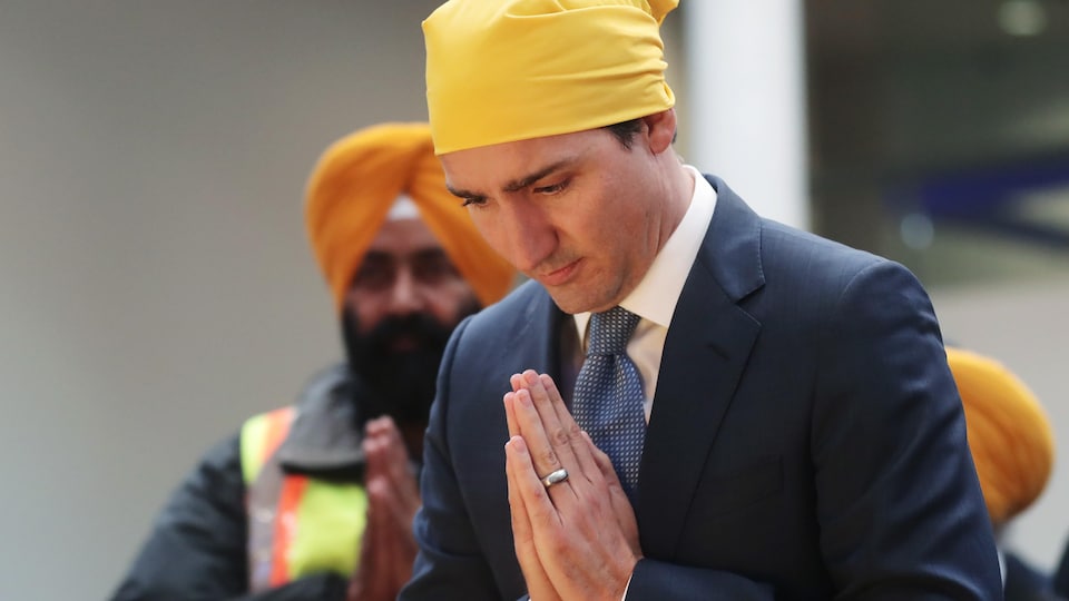 Justin Trudeau joint les mains et porte un turban sikh traditionnel.