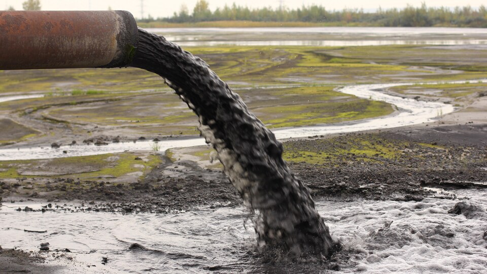 Un tuyau déverse de l'eau polluée sur un terrain vague.
