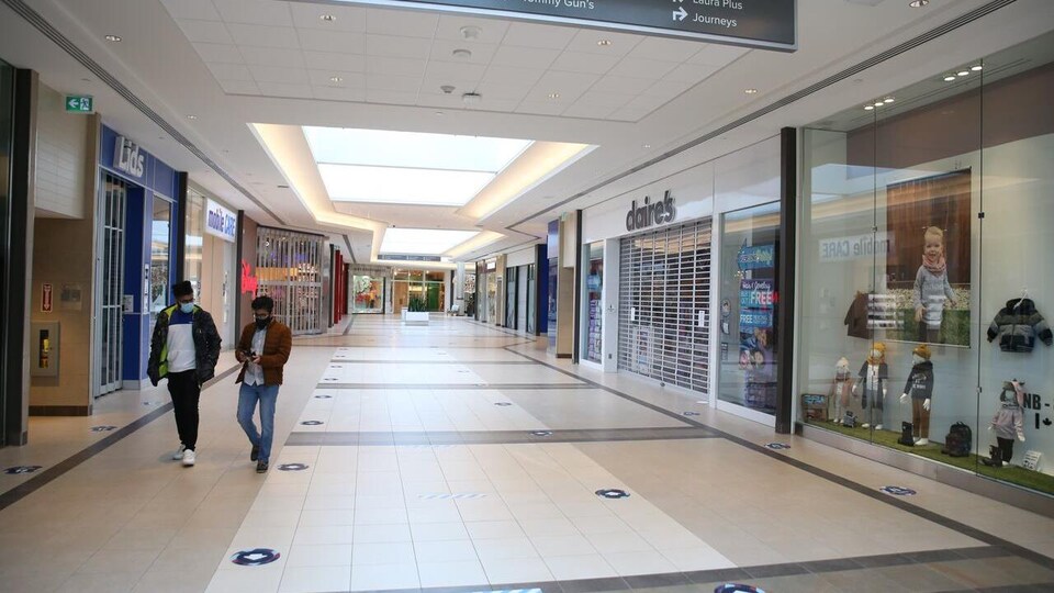 Deux personnes marchent dans un couloir vide, devant des commerces abandonnés.