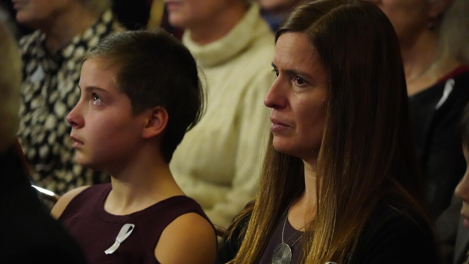 Une femme et une adolescente assistent à la cérémonie les yeux embués de larmes. 