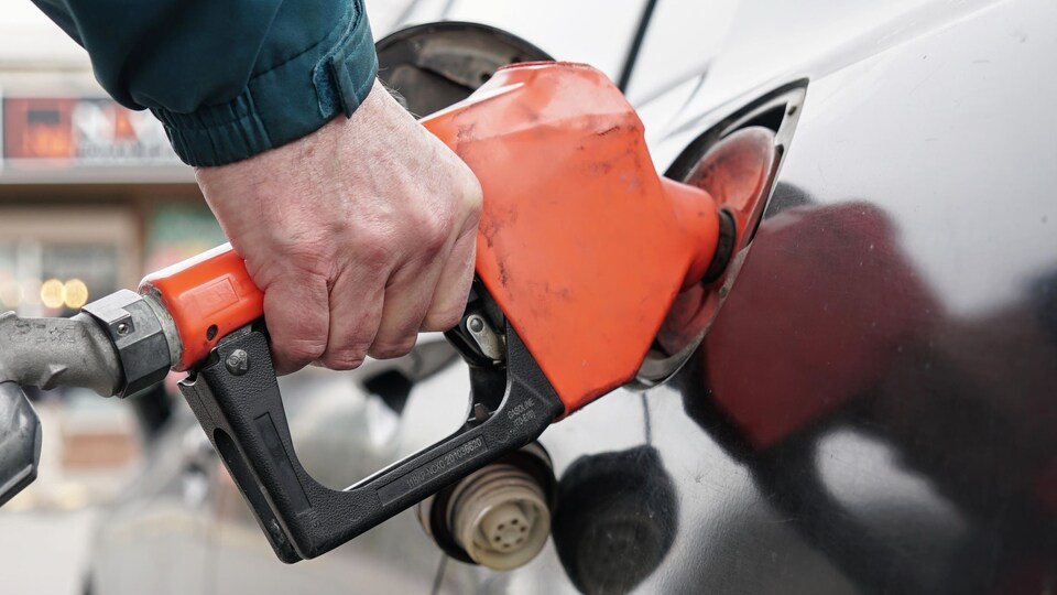 Une main tient un pistolet à essence versant du carburant dans une voiture.