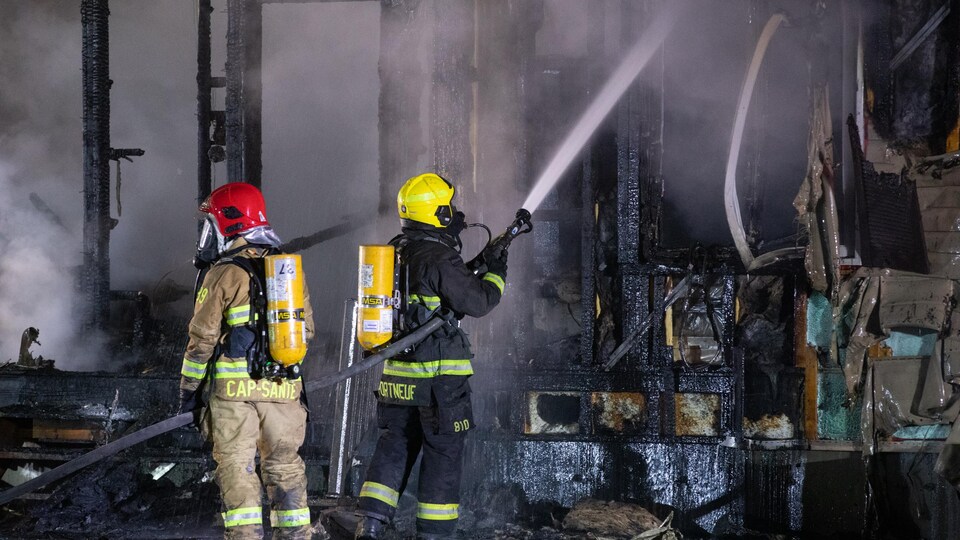 Deux pompiers devant la carcasse calcinée d'une résidence.