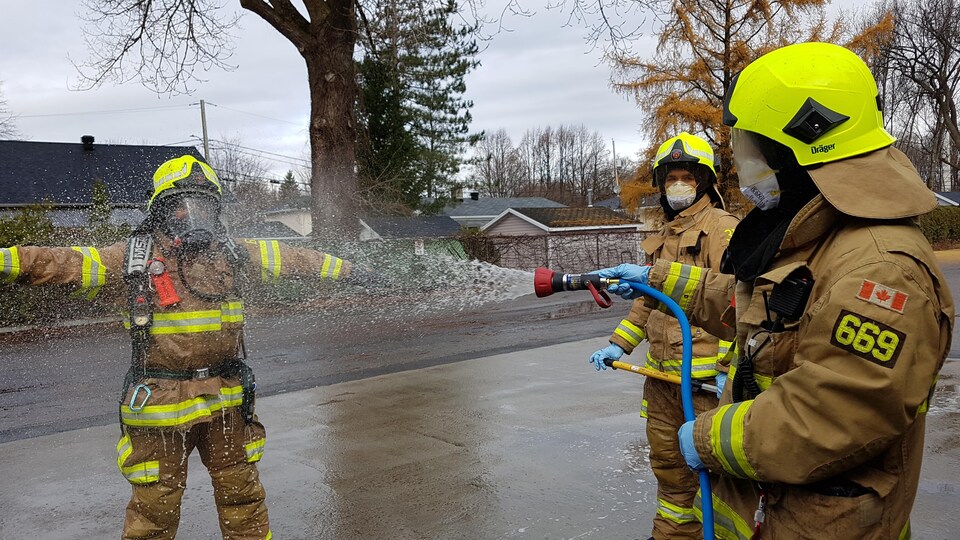 Un pompier rince l'équipement d'un collègue à l'aide d'un boyau d'arrosage sur les lieux d'un incendie.