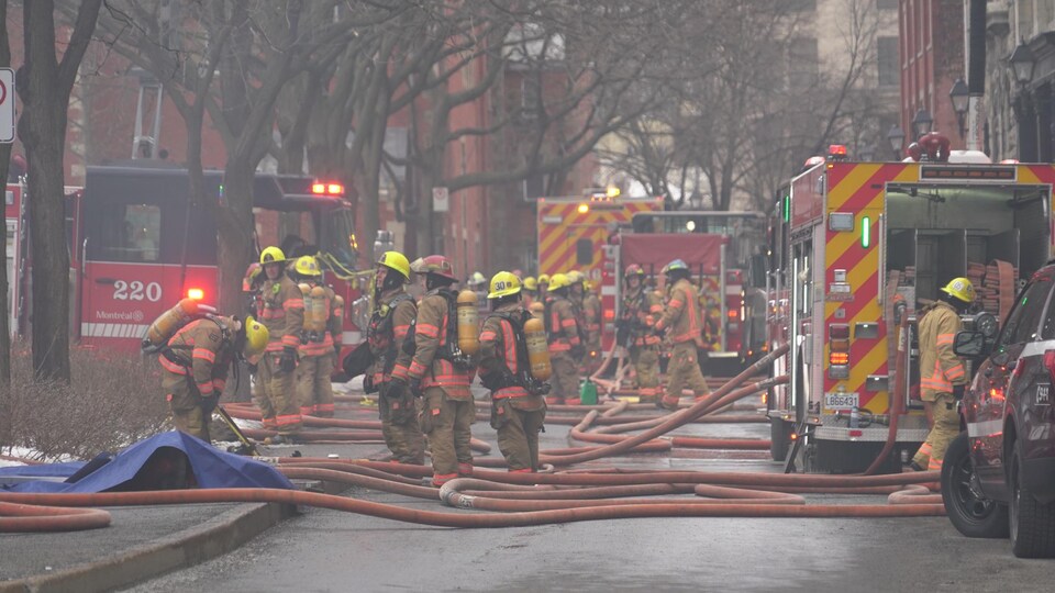 Des pompiers rassemblés dans la rue devant les camions d'incendie.                