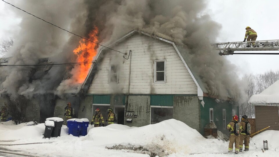 Plusieurs pompiers tentent d'éteindre un incendie ravageant un immeuble.