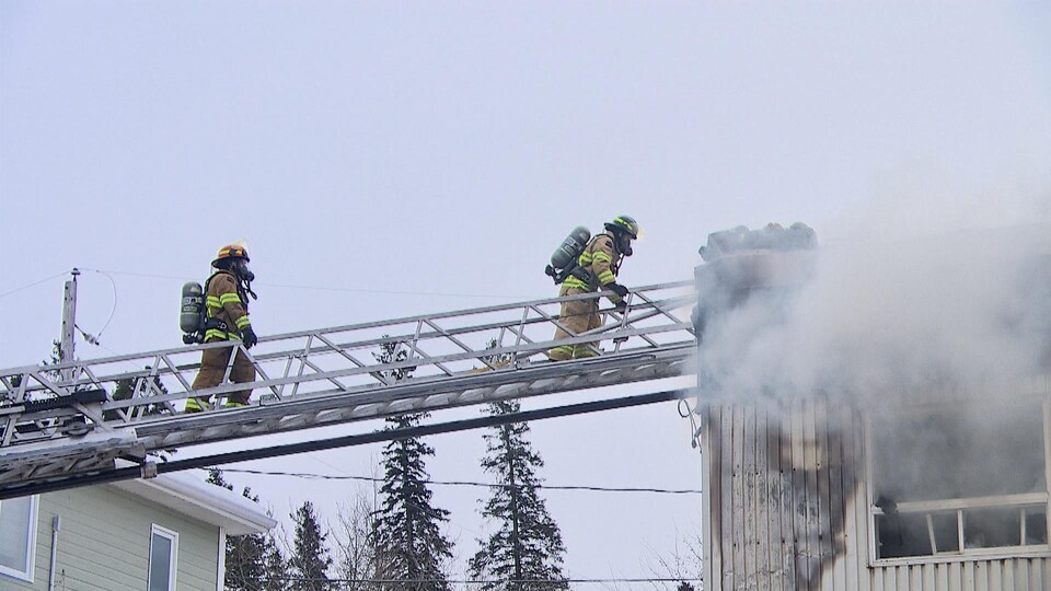 Des pompiers éteignent un incendie montés sur une échelle.
