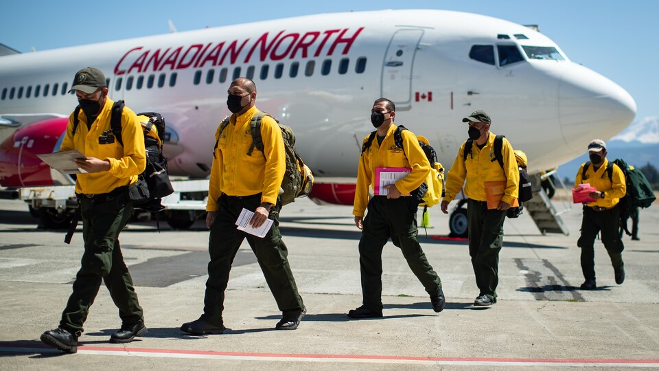 Les pompiers venus en renfort du Mexique marchent sur le tarmac de l'aéroport d'Abbotsford, à la sortie de l'avion.