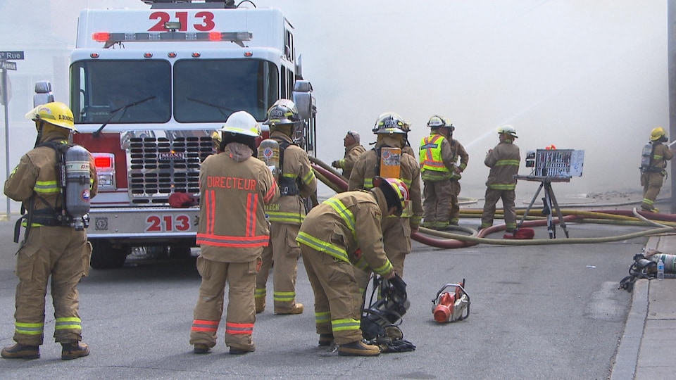 Des pompiers devant un camion de pompiers avec beaucoup de fumée