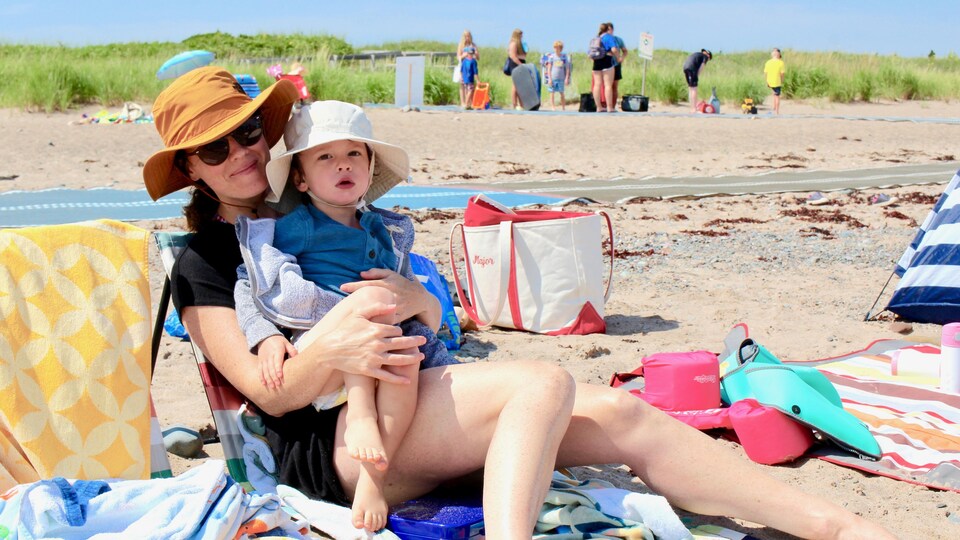 Jill Magor assise sur la plage tient son petit garçon sur ses genoux.