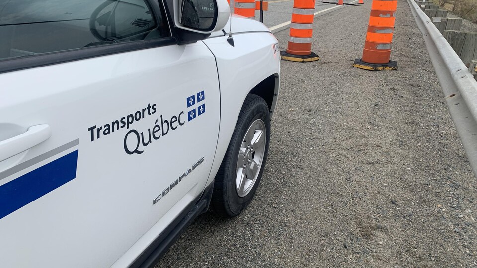 Une voiture du ministère des Transports est stationnée près du trou formé dans un ponceau.