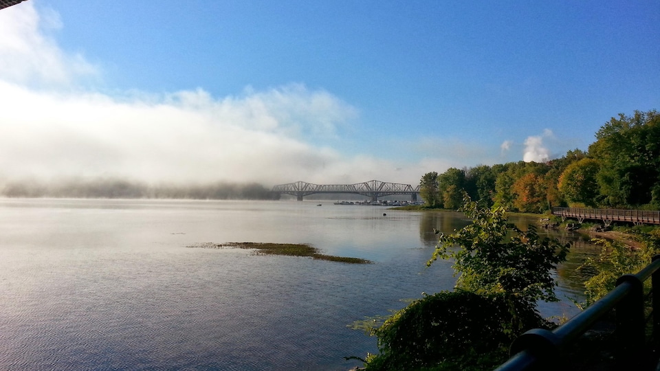 Le pont Alexandra qui enjambe la rivière de Outaouais, en matinée, avec la rive ontarienne couverte de brouillard.