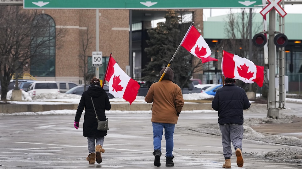 Trois manifestants avec des drapeaux devant l'entrée du pont.