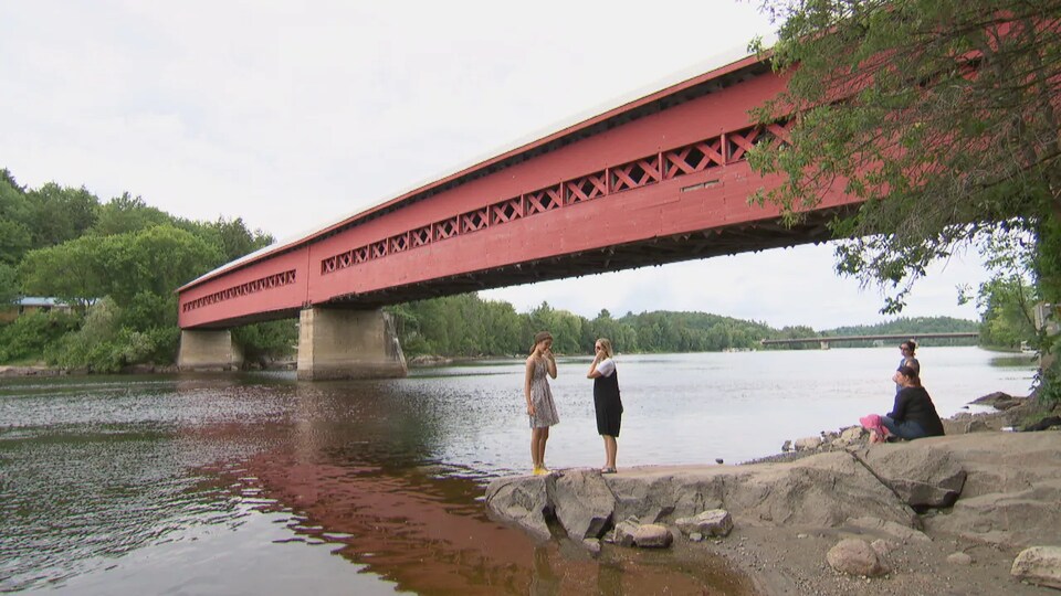 Des adolescents sont sur la rive près du pont couvert.