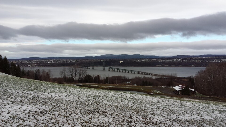 Le pont de l'Île-d'Orléans photographié au loin, depuis l'île d'Orléans. On aperçoit une fine couche de neige sur l'herbe.