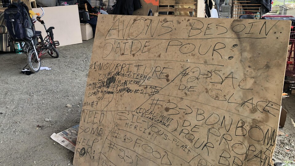 Une pancarte sur laquelle est écrit les besoins des personnes itinérantes : nourriture, sac de glace, bonbonne de propane, etc.
