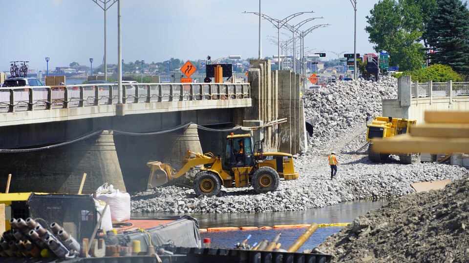 Des machines de construction circulent sur la rive en-dessous du pont. 