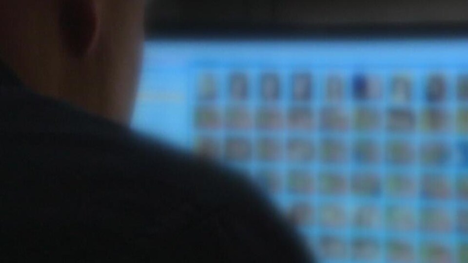 Un homme assis devant un écran couvert de visages floués.