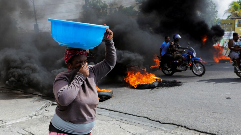 Une femme se couvre le nez et la bouche en passant devant un barrage routier en feu.