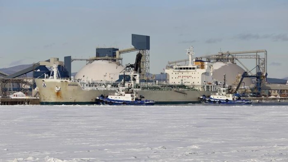 Deux remorqueurs procèdent à l'accostage d'un navire au Port de Québec en hiver.