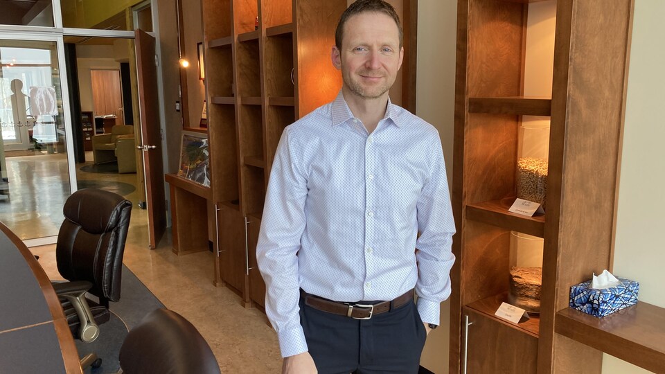 Un homme en chemise bleue sourit dans un bureau.