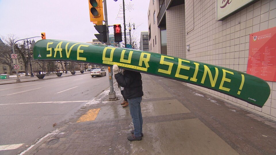 Un homme avec un canoë sur la tête, qui attend le signal pour traverser une artère principale de Winnipeg.