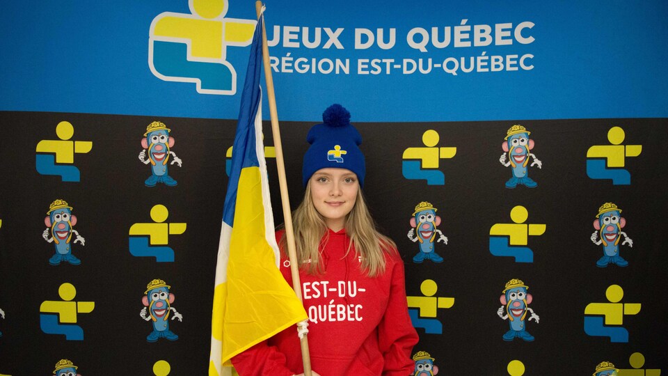 Une jeune femme porte un drapeau devant l'inscription « Jeux du Québec ».