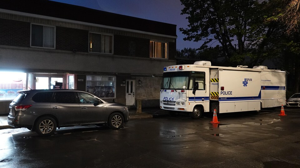 A large vehicle with the insignia of the Service de police de la Ville de Montréal parked in front of an apartment building at night.