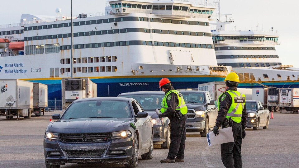 Des agents vêtus de vestes jaunes s'approchent des automobiles qui sortent du traversier amarré au quai.