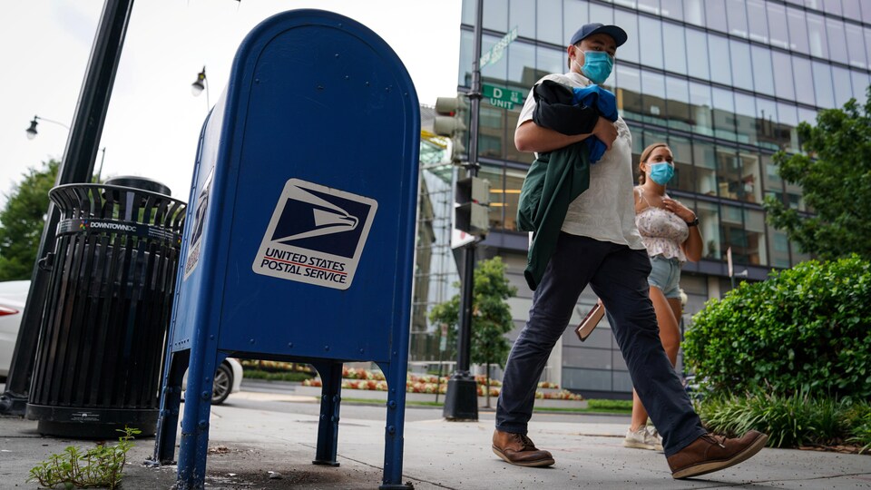 Un homme et une femme portant un masque marchent près d'une boîte postale.