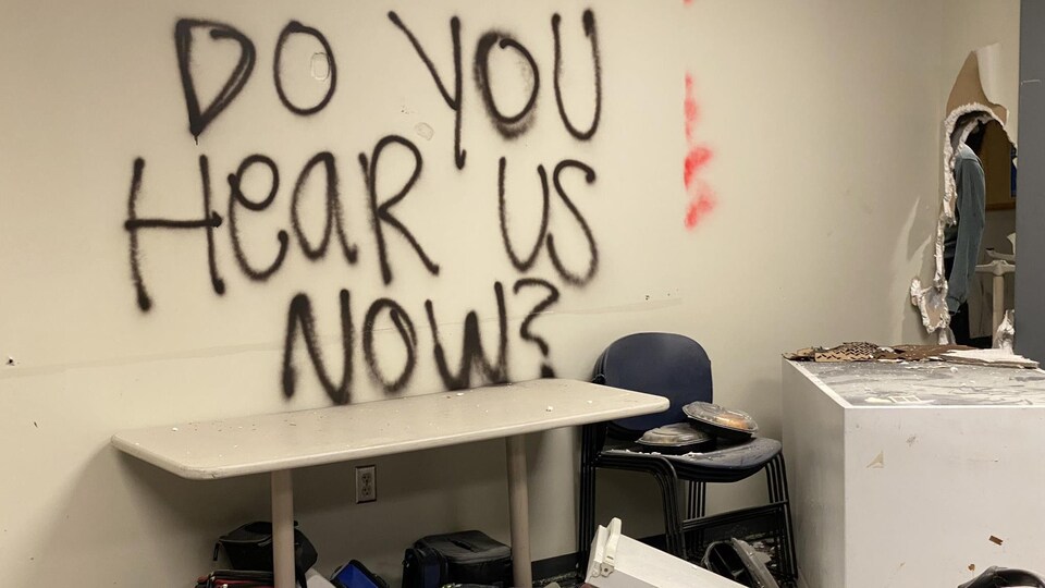 Une message en anglais écrit sur un mur à l'intérieur d'un commissariat de police saccagée dit : « Et maintenant, vous nous entendez? »