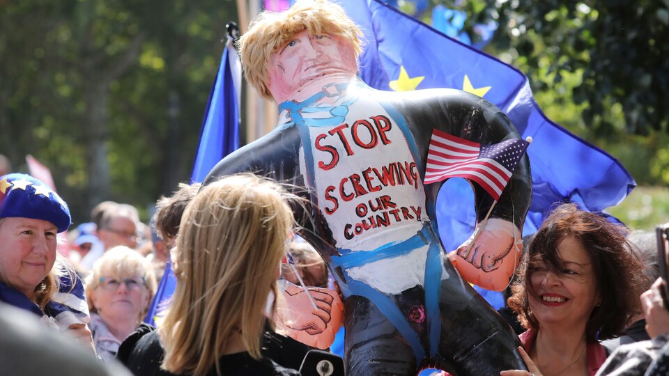 Deux femmes brandissent une poupée gonflable du premier ministre Johnson sur laquelle on peut lire : « Arrêtez de baiser notre pays ».