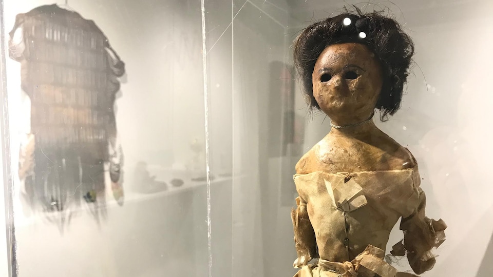 Une poupée de cire avec une robe et des cheveux bruns hmains dans une vitrine. 