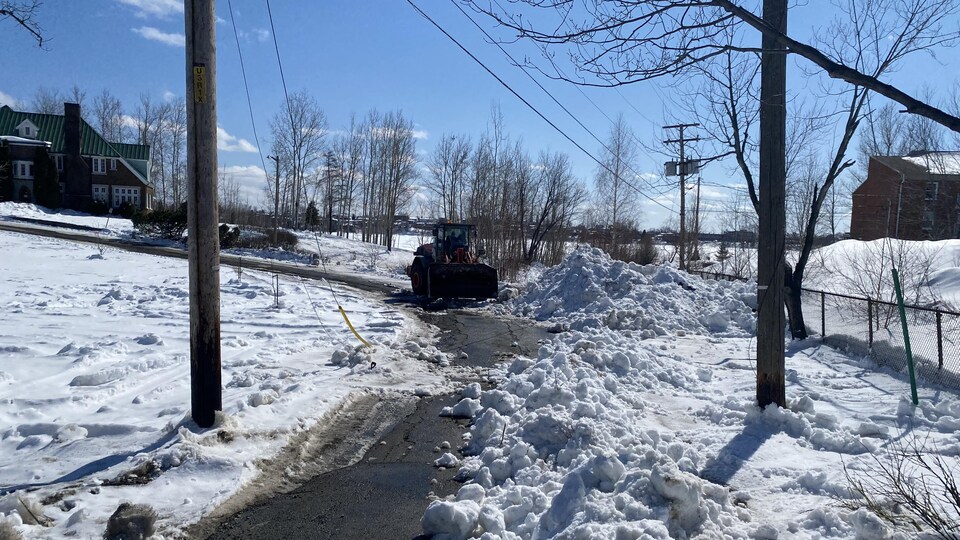 Un tracteur procède au déblaiement de la neige dans l'entrée en demi-cercle d'une bâtisse.