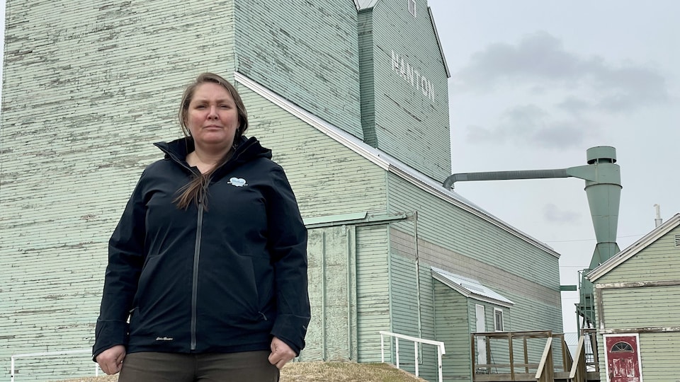 Amanda Bustard se tient debout devant deux silos à grains vert.