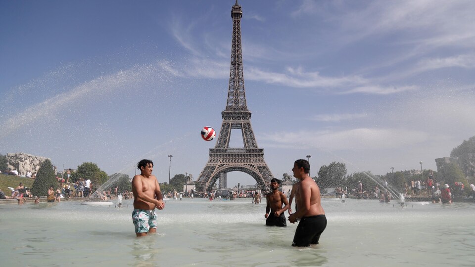 Des garçons jouent au ballon dans une fontaine devant la tour Eiffel.